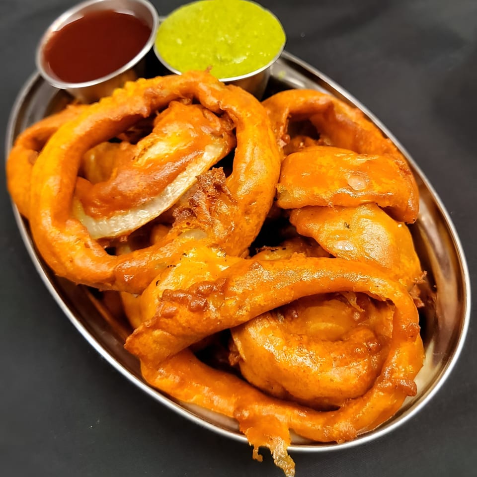 Crispy golden onion rings with two dipping sauces, red and green, on a silver platter.