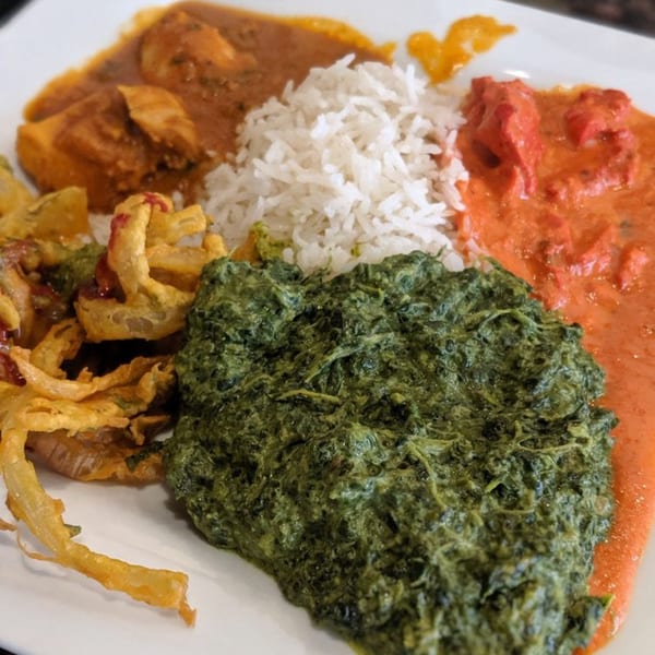 A vibrant Indian platter with rice, saag, chicken tikka masala, and pakora on a white plate.
