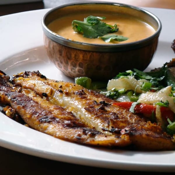 Grilled fish fillet with a side of mixed vegetables and a bowl of creamy sauce.