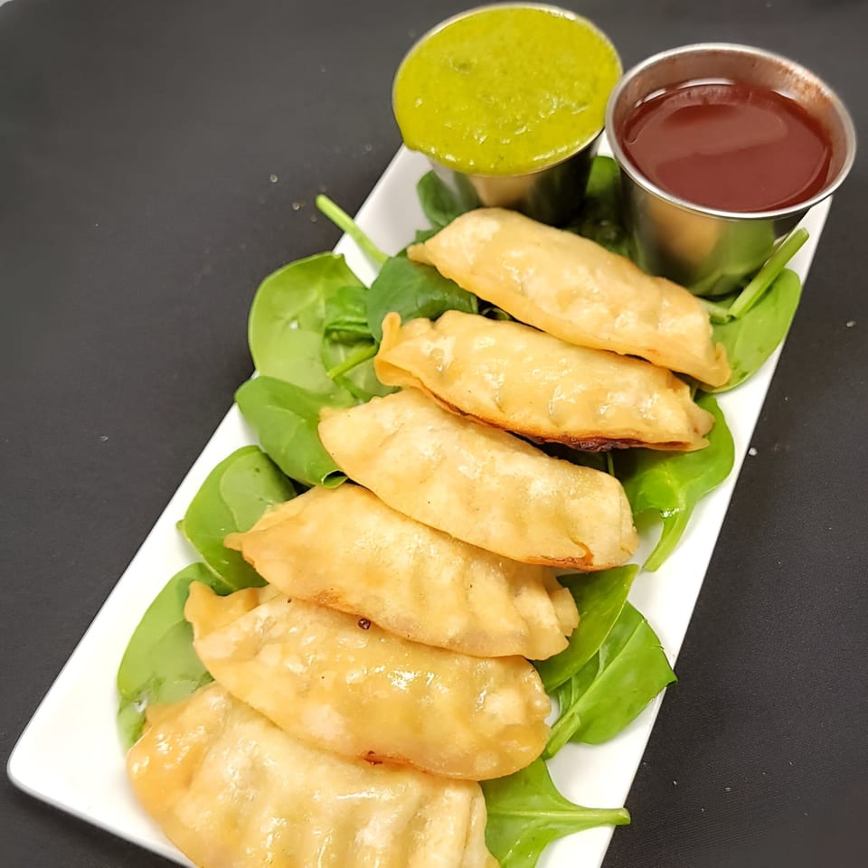 Fried dumplings on a bed of spinach with green and red dipping sauces on a white plate.